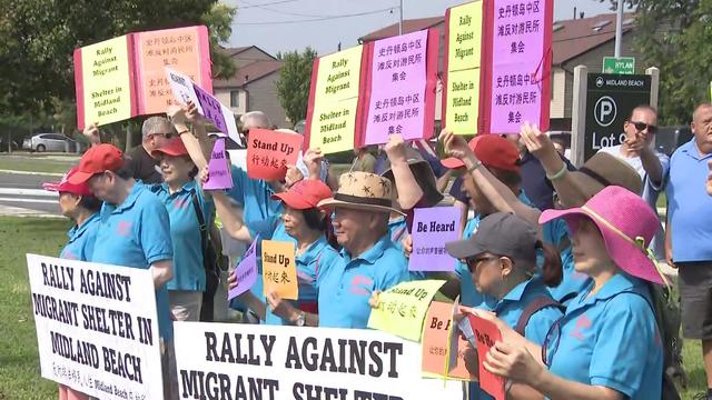 Protesters hold signs that say "Rally against migrant shelter in Midland Beach." 