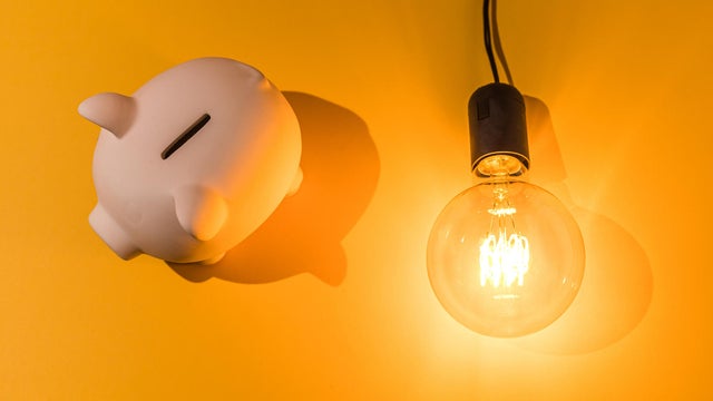 Piggy bank next to lit light bulb on pink background. Concept of electricity price, crisis, money, saving and power energy. 