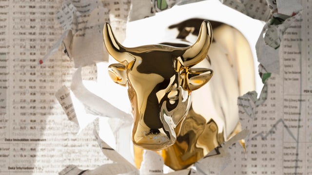 A golden bull breaking through the finance section of a newspaper 