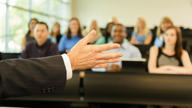 Education: Professor with college students in lecture hall classroom. 