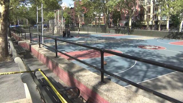 NYPD officers stand on a park basketball court blocked off by crime scene tape. 