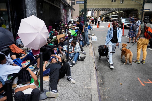 Migrants sit in a queue outside of The Roosevelt Hotel that is being used by the city as temporary housing on Monday, July 31, 2023, in New York.