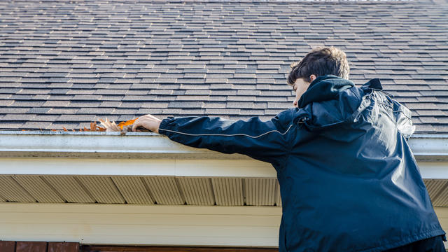 Teenage boy removing leaves from gutter during day 