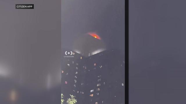 Flames can be seen at the top of a 30-story apartment building. 