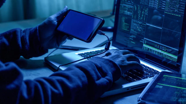 Hacker with mobile phone and computer in a dark room. Cyber crime  concept. 