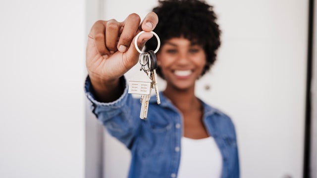 Happy woman showing house keys standing in front of door 