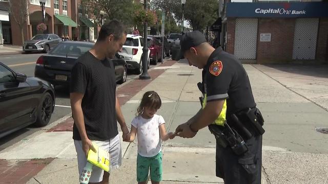 A Suffolk County Police officer hands a child a reflective sticker after handing a man a reflective vest. 