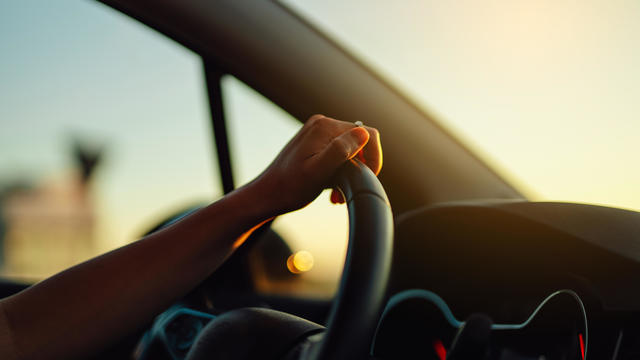 Female hand holding steering wheel in a car during a drive at sunset 
