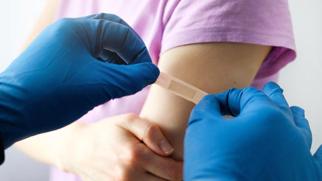 A gloved doctor applies a Band-Aid after vaccination 