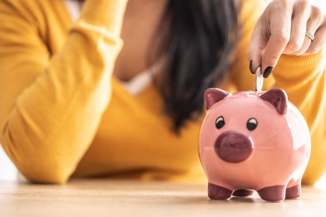 A woman's hand puts a coin into a piggy bank.