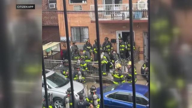 Numerous firefighters stand outside a Queens apartment building. 