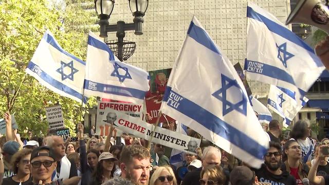 Protesters crowd a street, many holding Israeli flags. 