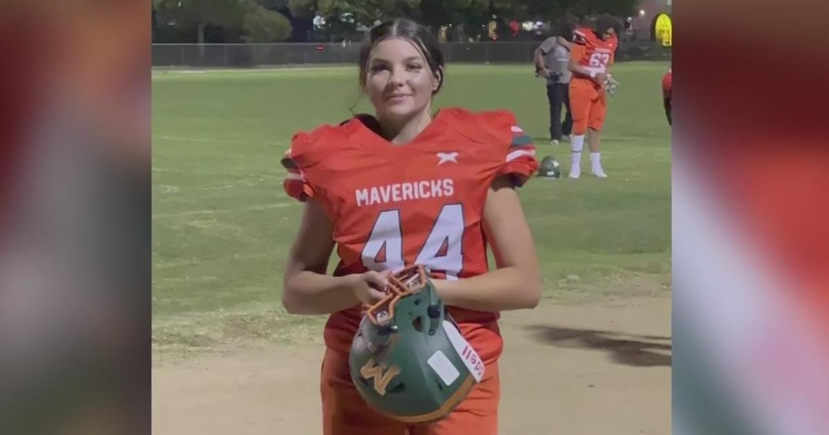 Senior boy wearing football jersey and holding football in front of blue  lockers in Oak View High School El Dorado HIlls