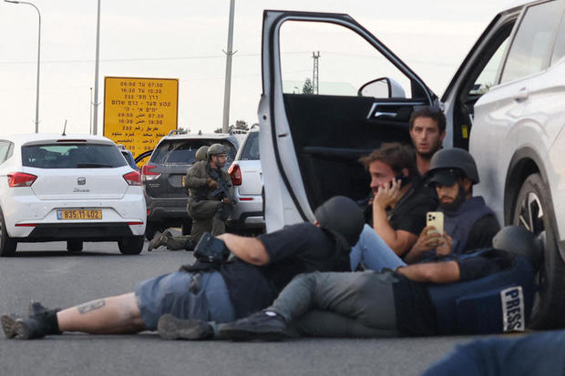 Journalists take cover behind cars as Israeli soldiers take position during clashes with Hamas fighters near the Gevim kibbutz, close to the border with Gaza on October 7, 2023. 