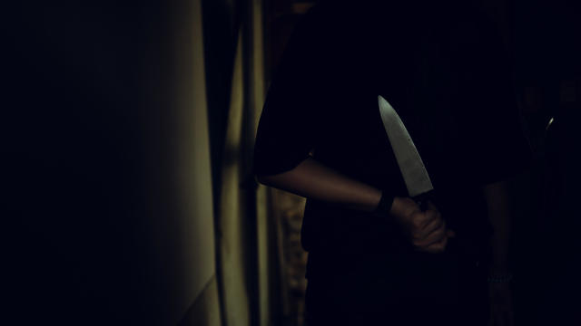 The shadow of a female murderer stood terrifyingly holding a knife and lit from behind.Scary horror or thriller movie mood or nightmare at night Murder or homicide concept. 