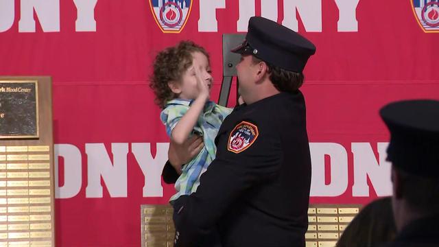 An FDNY firefighter holds a 5-year-old boy in his arms on a stage. 
