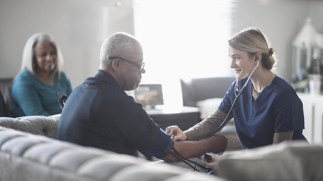 Nurse taking patient blood pressure in living room 