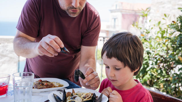 Father helping his toddler son to clean mussels at a terrace of a restaurant 