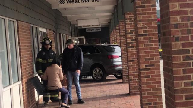 An SUV can be see on the walkway in front of a row of stores. 