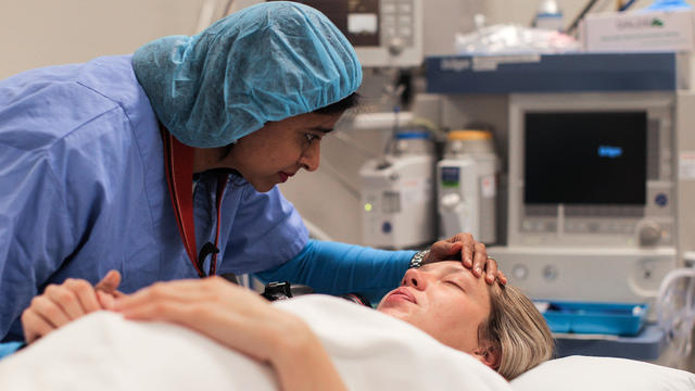a Doula supports and comforts her emotional pregnant client as she lays in the operating theatre. 