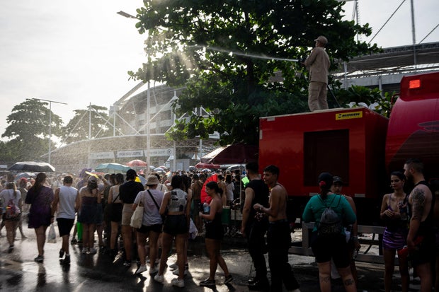 A firefighter cools off Taylor Swift fans with a hose as they queue outside the Nilton Santos Olympic Stadium amid a heat wave in Rio de Janeiro on November 18, 2023.