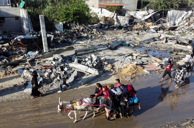 Displaced Palestinians return to their homes as they pass by a house destroyed in an Israeli strike during the conflict, amid the temporary truce between Hamas and Israel, in Khan Younis