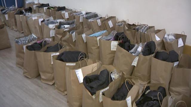 Dozens of brown paper bags stuffed with coats sit on a floor. 