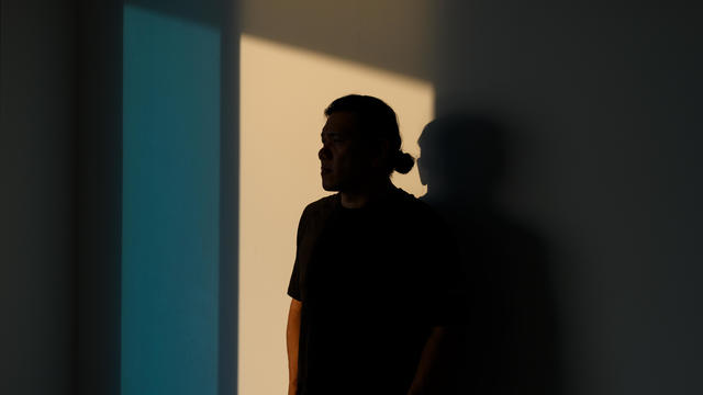 A man, completely obscured in shadow, looks away 