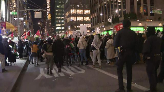 A large crowd of protesters walk down Sixth Avenue, following by police officers. 