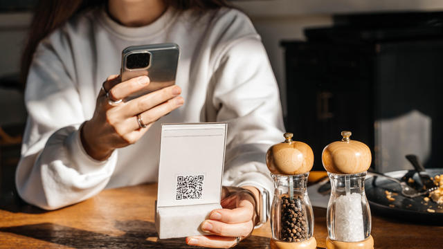 A beautiful young woman with long hair scans a QR code in a café to see the menu online. 