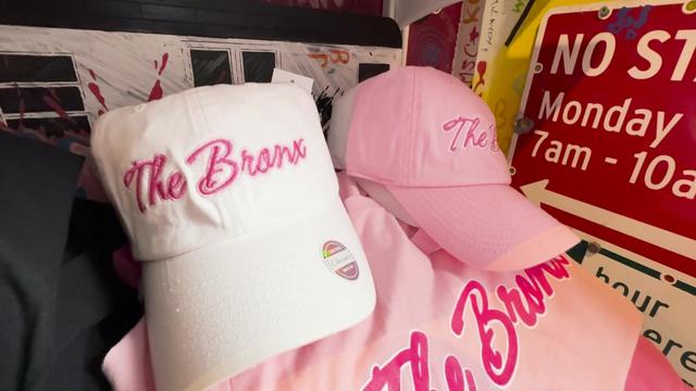 Clothing items for same in the shop Bronx native, including a white baseball hat that reads "The Bronx" in pink cursive, a pink baseball hat that reads "The Bronx" in dark pink cursive and a pink shirt that reads "The Bronx" in dark pink cursive. 