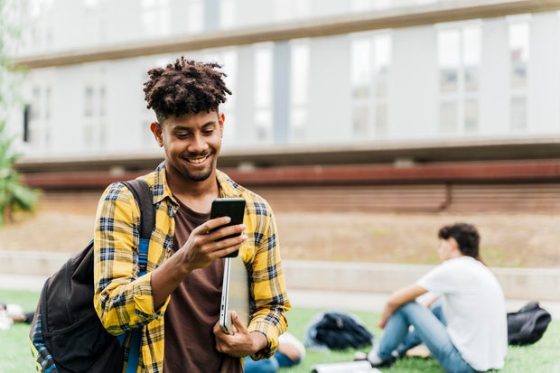 College student on college campus walking and looking at smart phone holding laptop. Concept of students and technology. 