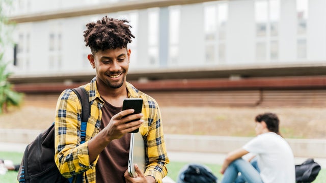 College student on college campus walking and looking at smart phone holding laptop. Concept of students and technology. 