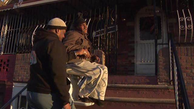 18-year-old Niem sits in a stair lift to reach his front porch as his father stands nearby. 