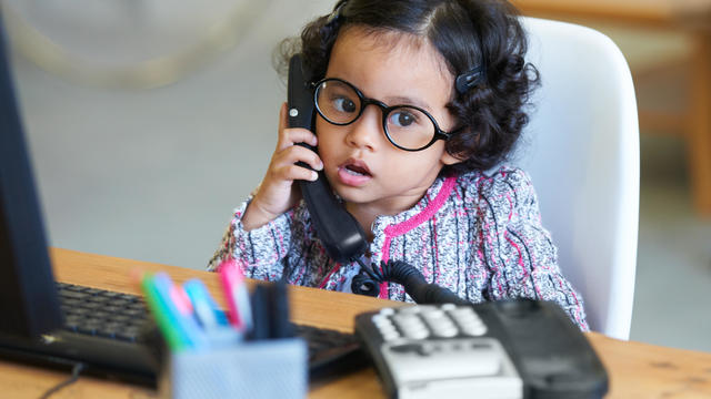 A little girl sitting in front of a computer while talking on the phone 