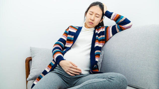 a pregnant woman suffering from sickness while sitting on couch 