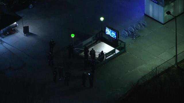 An aerial view of Utica Avenue subway station at night. Several NYPD officers stand near the entrance. 