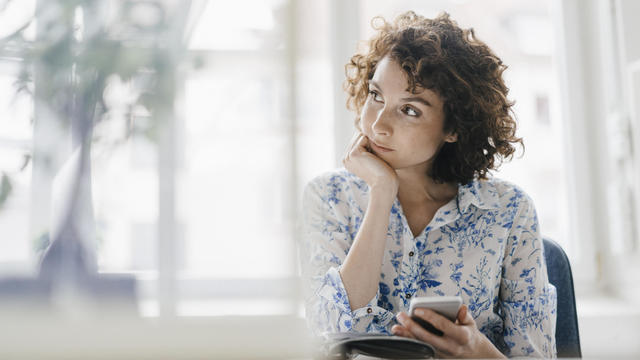 Businesswoman in office with smartphone and diary, looking worried 