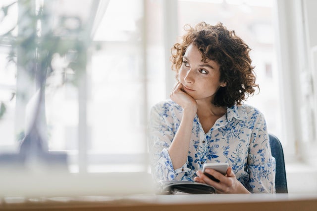 Businesswoman in office with smartphone and diary, looking worried 