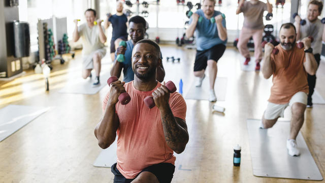 Smiling male fitness instructor practicing dumbbell exercise with men in gym 