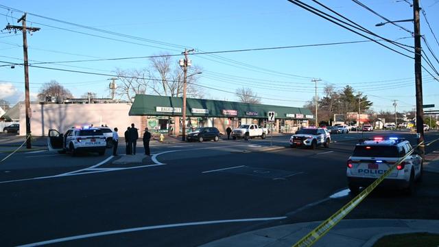 Crime scene tape blocks off a street in Farmingdale. Multiple police vehicles are parked on the street. 