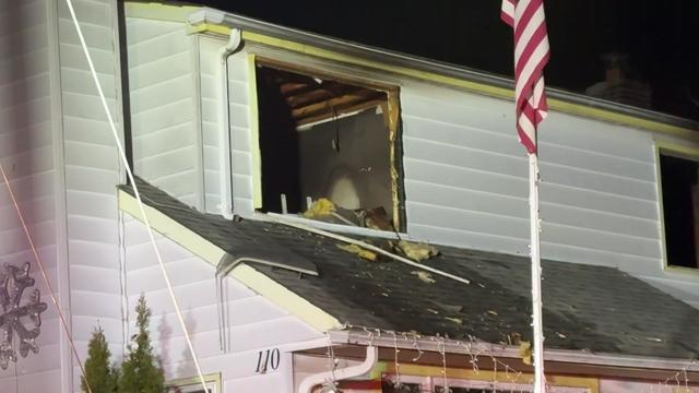 A second-floor window on a two-story home has been broken, exposing smoke and fire damage inside. 