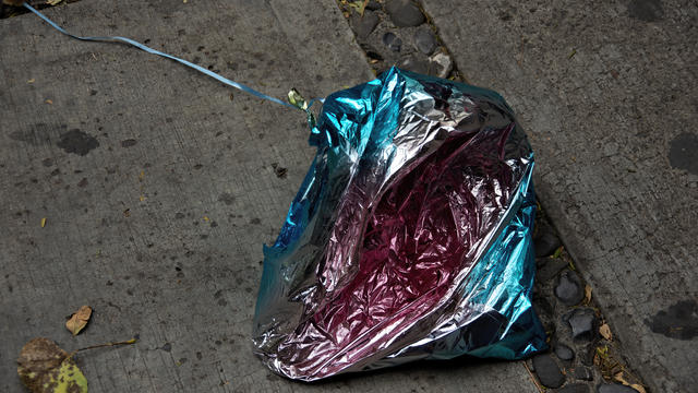 Deflated foil balloon littering a dirty concrete sidewalk 