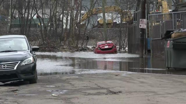 Vehicles parked on a street in shallow flood waters. 