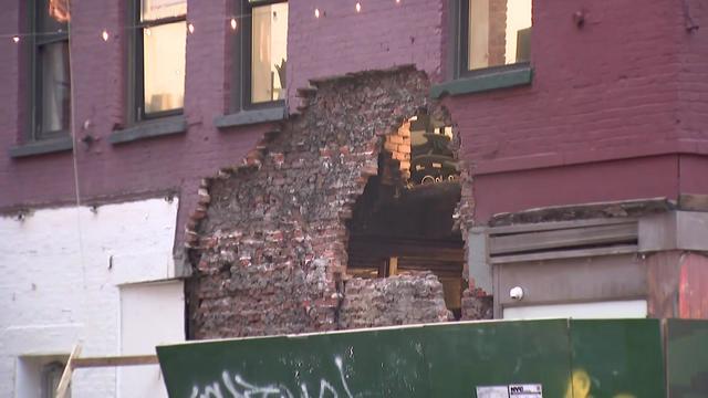 The exterior of a building in Little Italy. A facade has partially collapsed, revealing a hole in the exterior wall. 