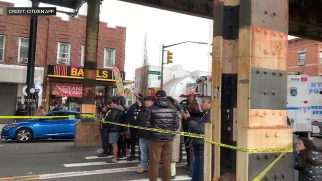 Onlookers stand behind crime scene tape underneath elevate subway tracks in Brooklyn. 