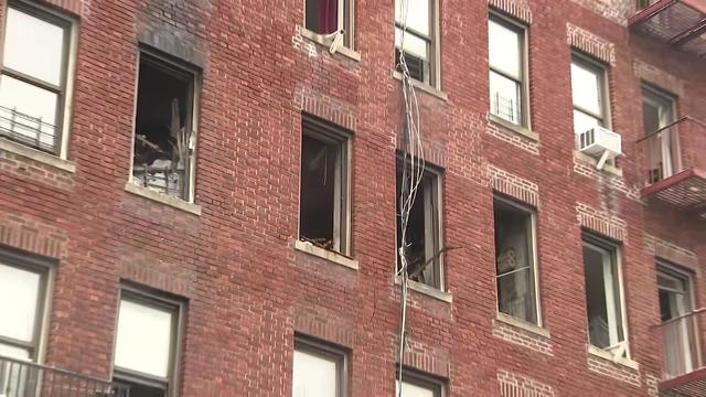 The exterior of a Bronx apartment building. Multiple windows have been broken and smoke and fire damage can be seen outside and inside the building. 