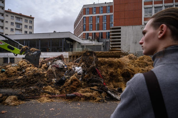 A bystander watches as farmers from the Midi-Pyrenees region of southwest France dump manure and rotting produce outside a government administrative building as they take part in a protest against taxation, declining income and difficult work conditions, in central Toulouse, Jan. 16, 2024