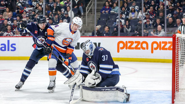 Goaltender Connor Hellebuyck #37 of the Winnipeg Jets makes a save as Adam Lowry #17 and Bo Horvat #14 of the New York Islanders battle during first period action at the Canada Life Centre on January 16, 2024 in Winnipeg, Manitoba, Canada. 