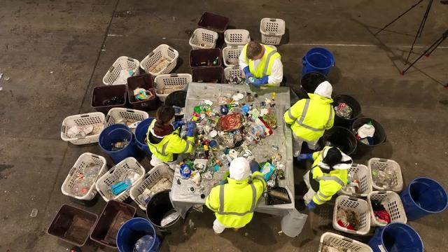 An overhead view of five individuals sorting through a large pile of recyclables. 